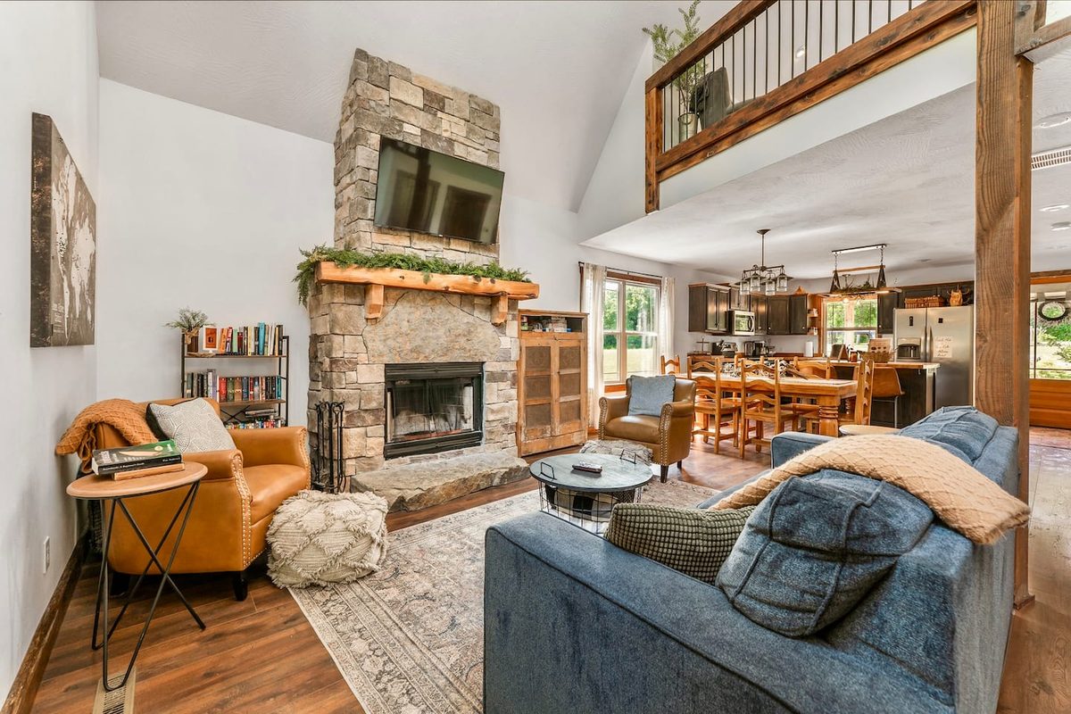 Vaulted living room with a floor-to-ceiling stone fireplace, mounted TV and open sightlines to the dining area