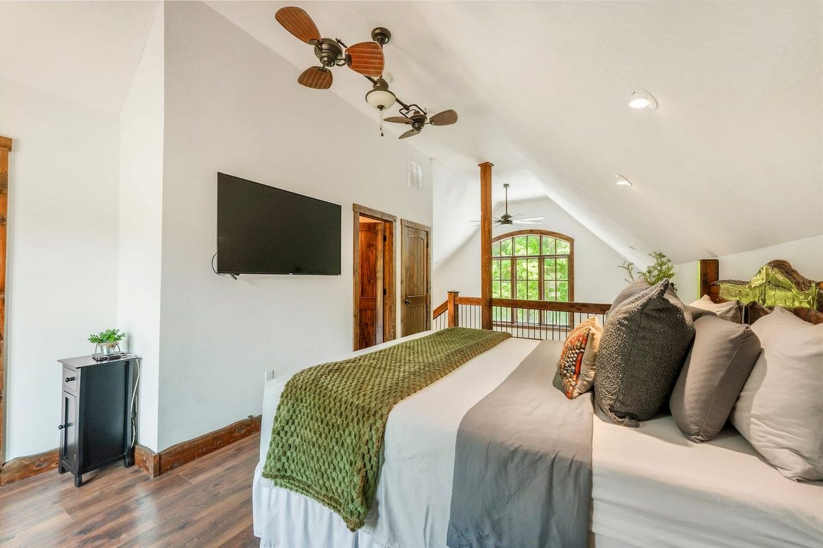 Loft bedroom with a vaulted ceiling, ceiling fan and mounted TV
