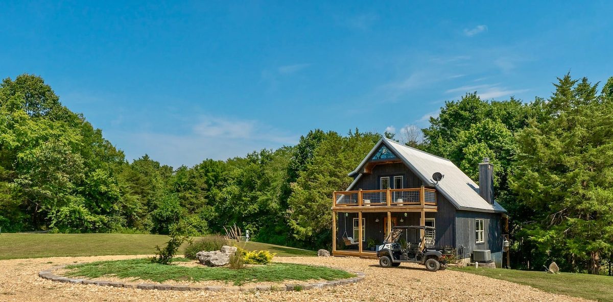 The cabin on a clear day with the UTV parked beside the gravel drive